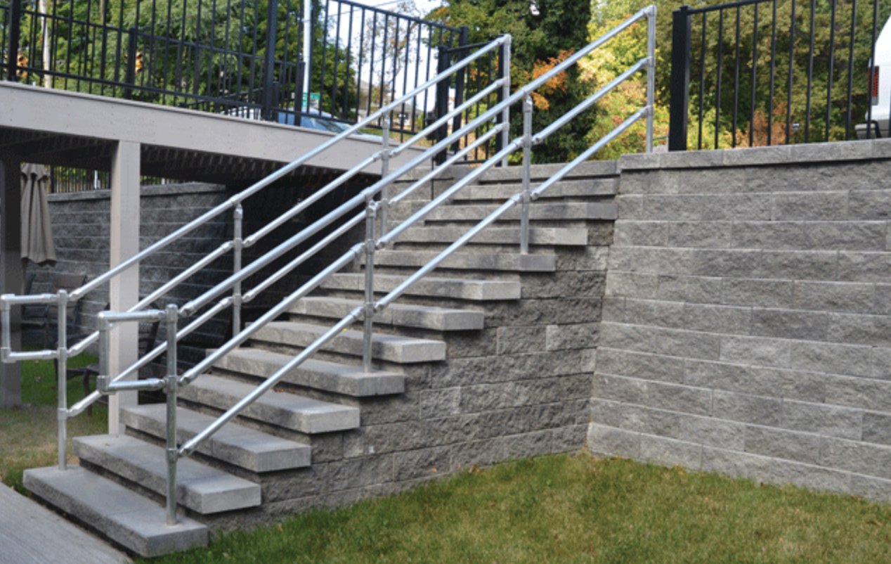Keystone block staircase with steel handrails built into a retaining wall beside a raised deck