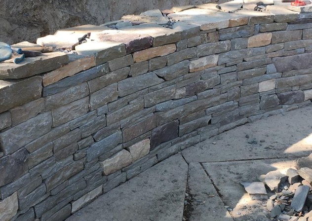Curved stone wall with natural bluestone caps under construction