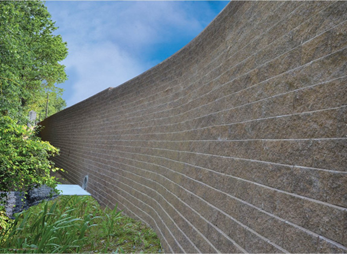 Tall curved Keystone segmental retaining wall rising along a wooded slope