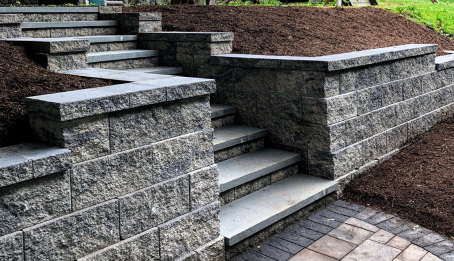 Terraced Keystone retaining walls with capped block steps climbing a mulched hillside