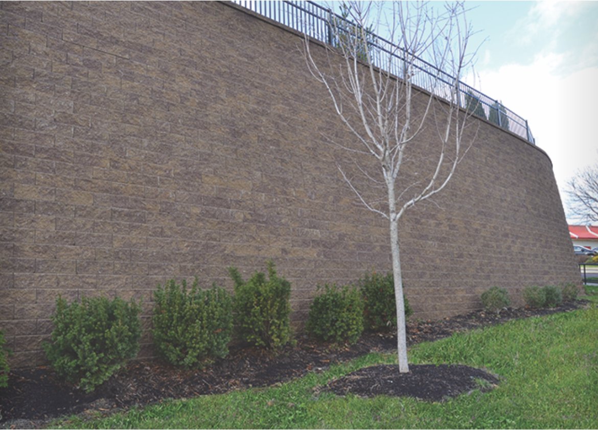 Tall curved commercial Keystone retaining wall with railing above a landscaped bed