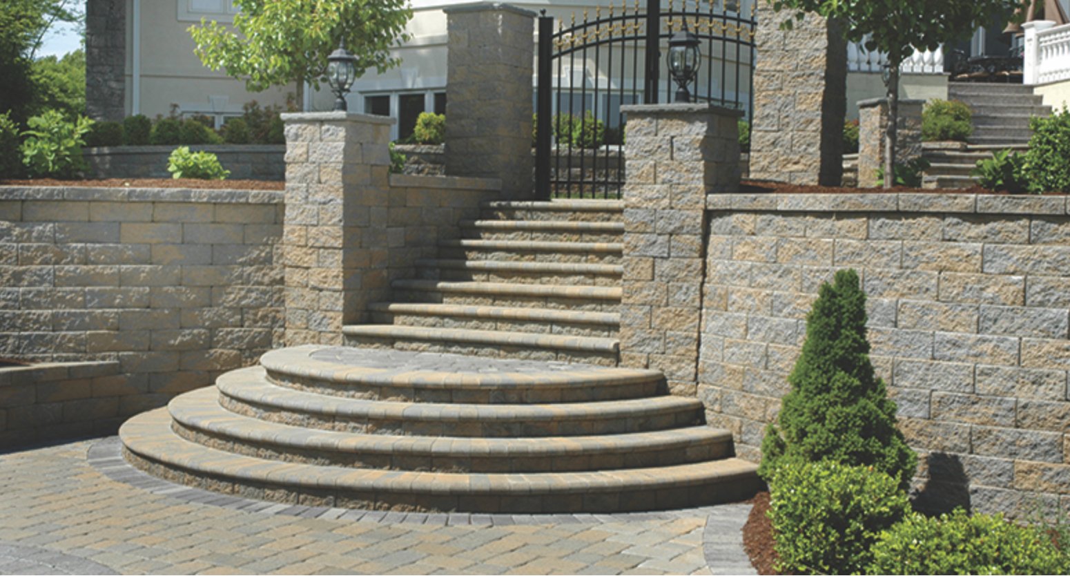 Curved Keystone block steps flanked by capped pillars and retaining walls leading to an iron entry gate