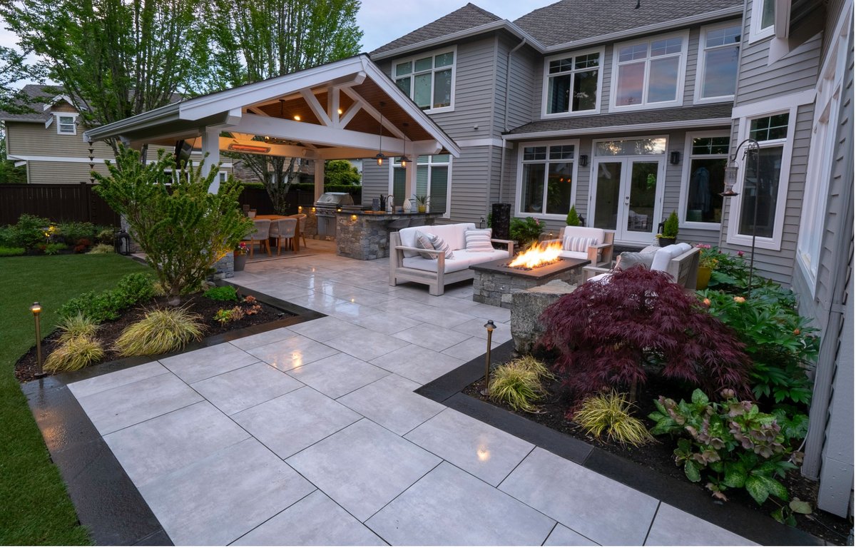 Large-format MSI porcelain paver patio with fire pit, lounge seating and covered outdoor kitchen at dusk