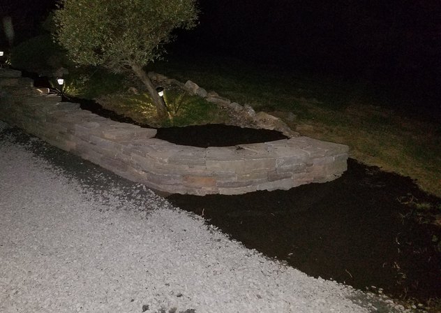 Stacked stone planter wall along a gravel driveway at night