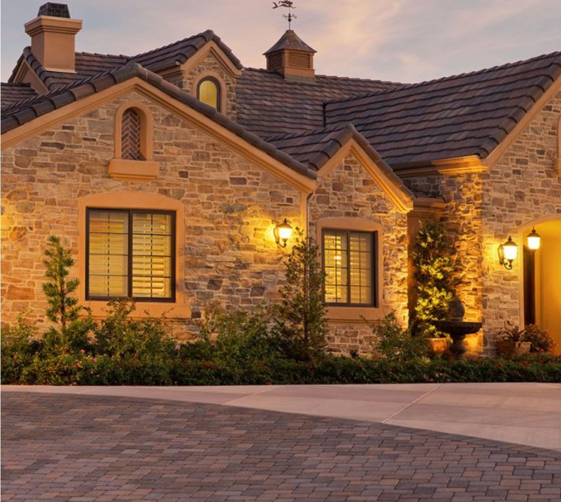 Stone cottage home clad in Eldorado Stone veneer, lit by lanterns at dusk