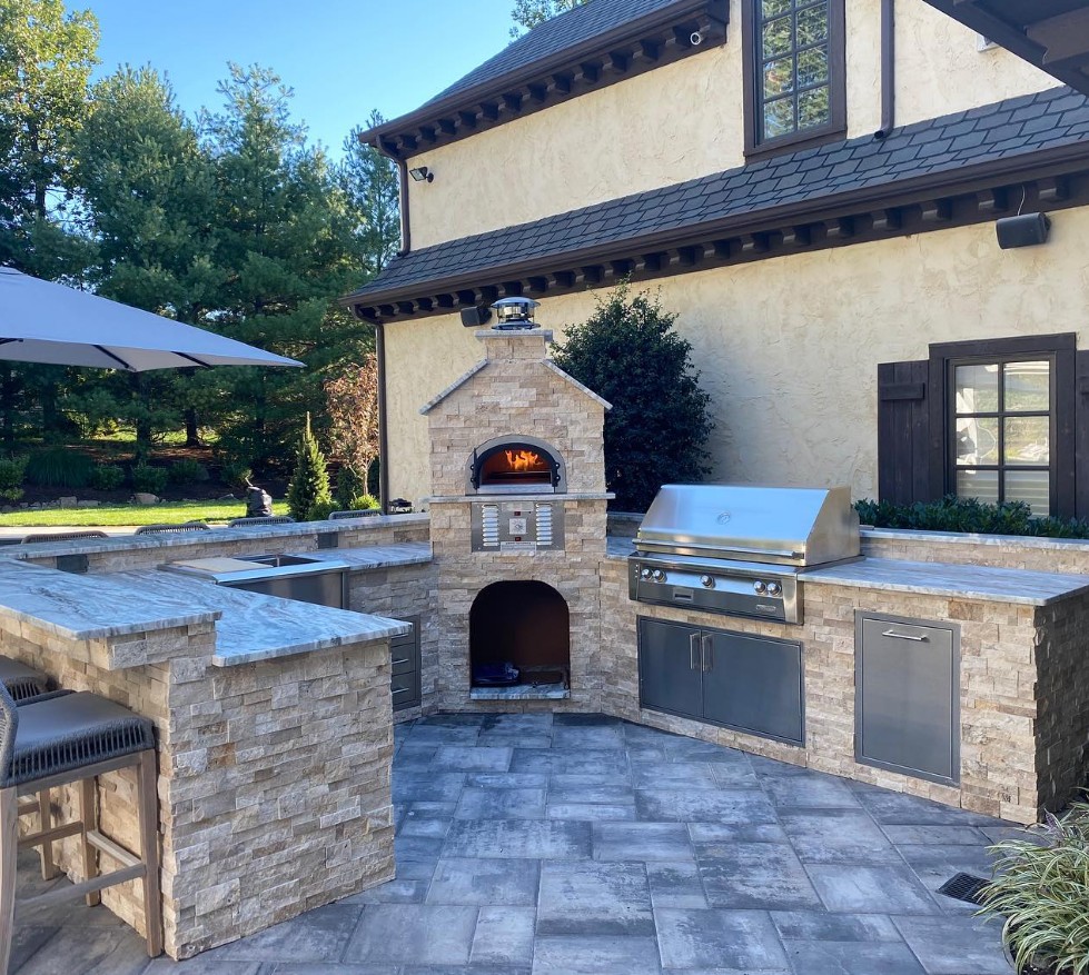 Outdoor kitchen with a stacked stone pizza oven, grill and bar seating