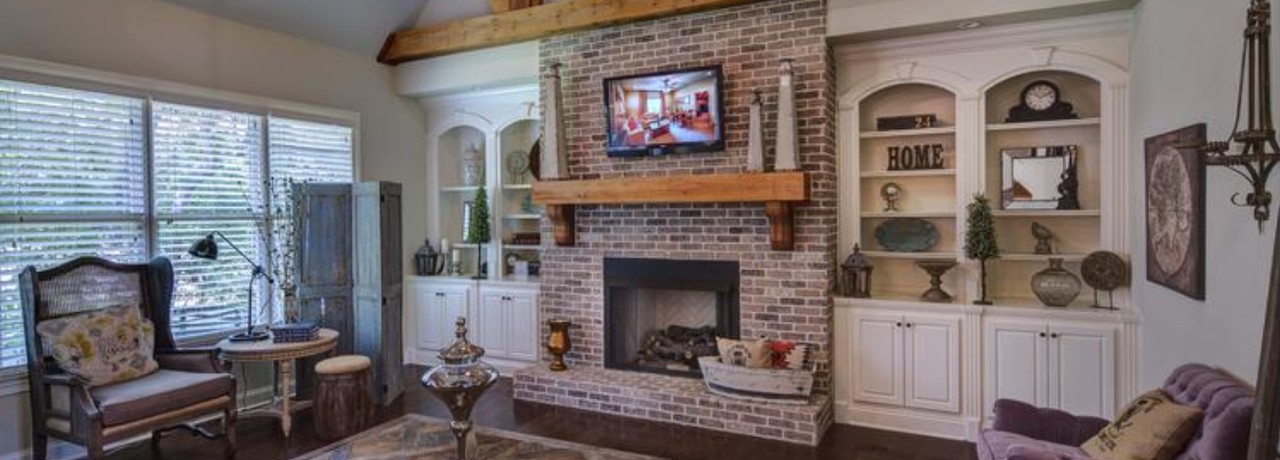Living room fireplace and chimney wall finished in thin brick with a rustic wood mantel and beams