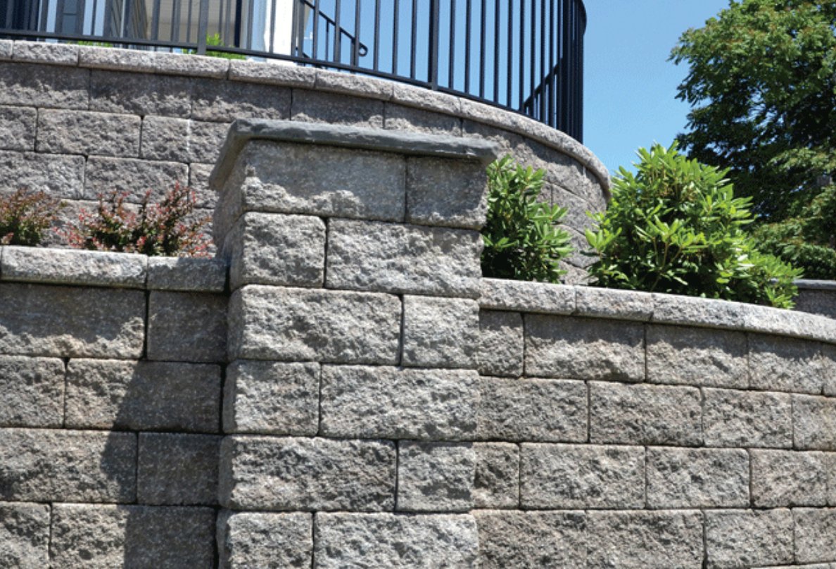 Tiered Keystone retaining wall with capped pillar and curved upper wall beneath a deck railing