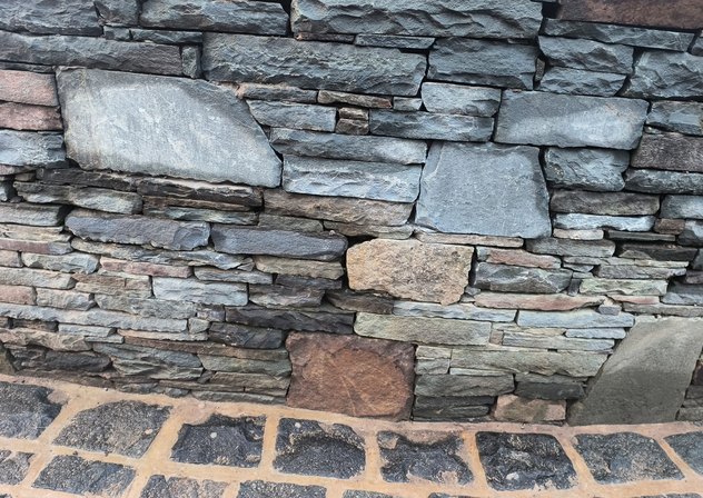 Dry-stacked bluestone wall above black granite cobblestone paving