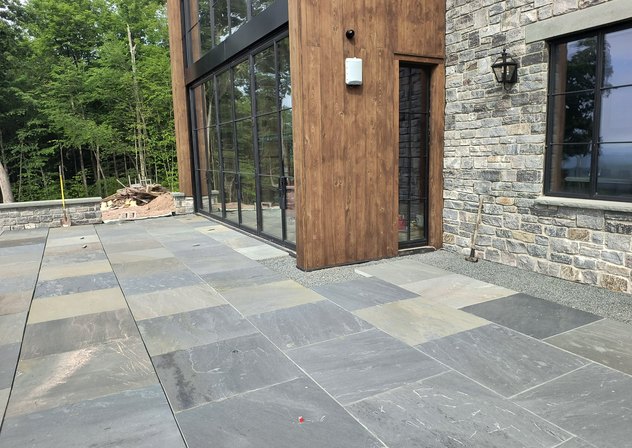 Full color bluestone pattern patio beside a modern stone and wood home
