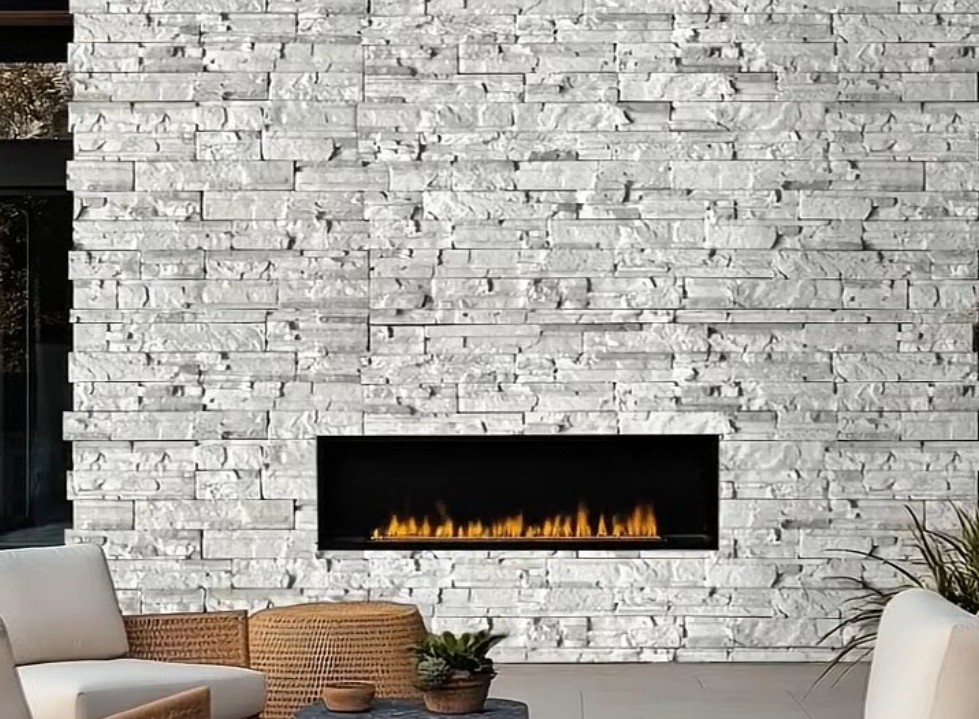 Outdoor linear fireplace set in a white stacked stone wall