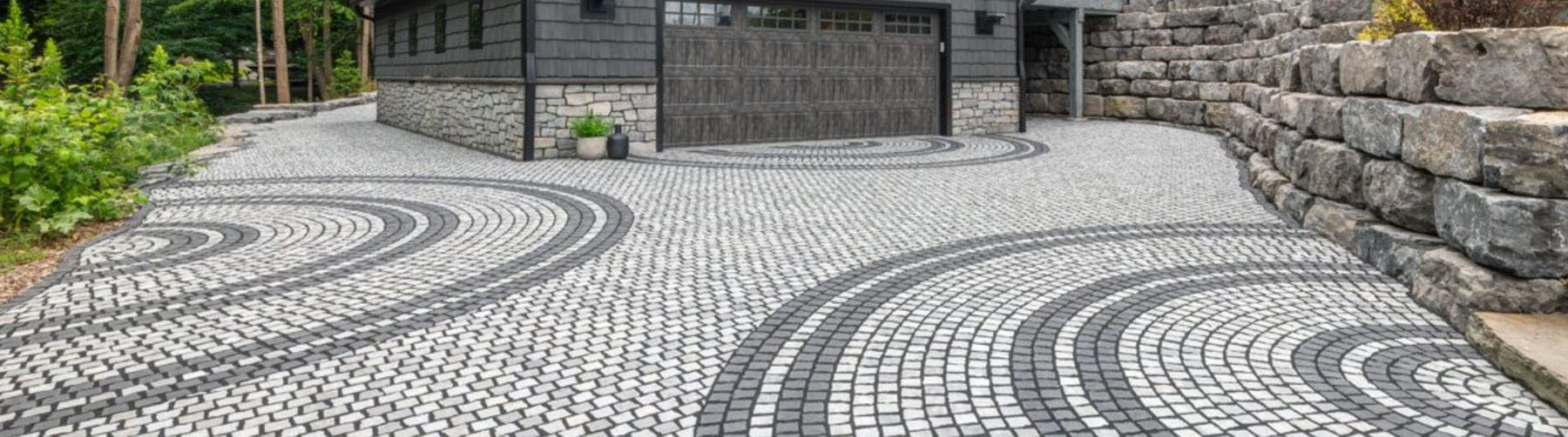 Circular paver driveway with radial pattern beside a stone retaining wall and home
