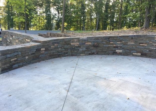 Curved dry-stacked stone retaining wall around a concrete pad