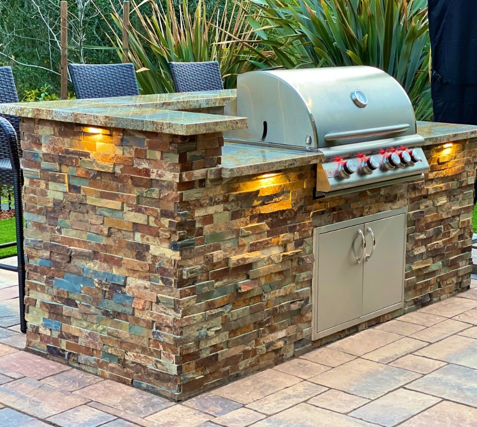 Outdoor grill island clad in multicolor natural stacked stone with under-counter lights