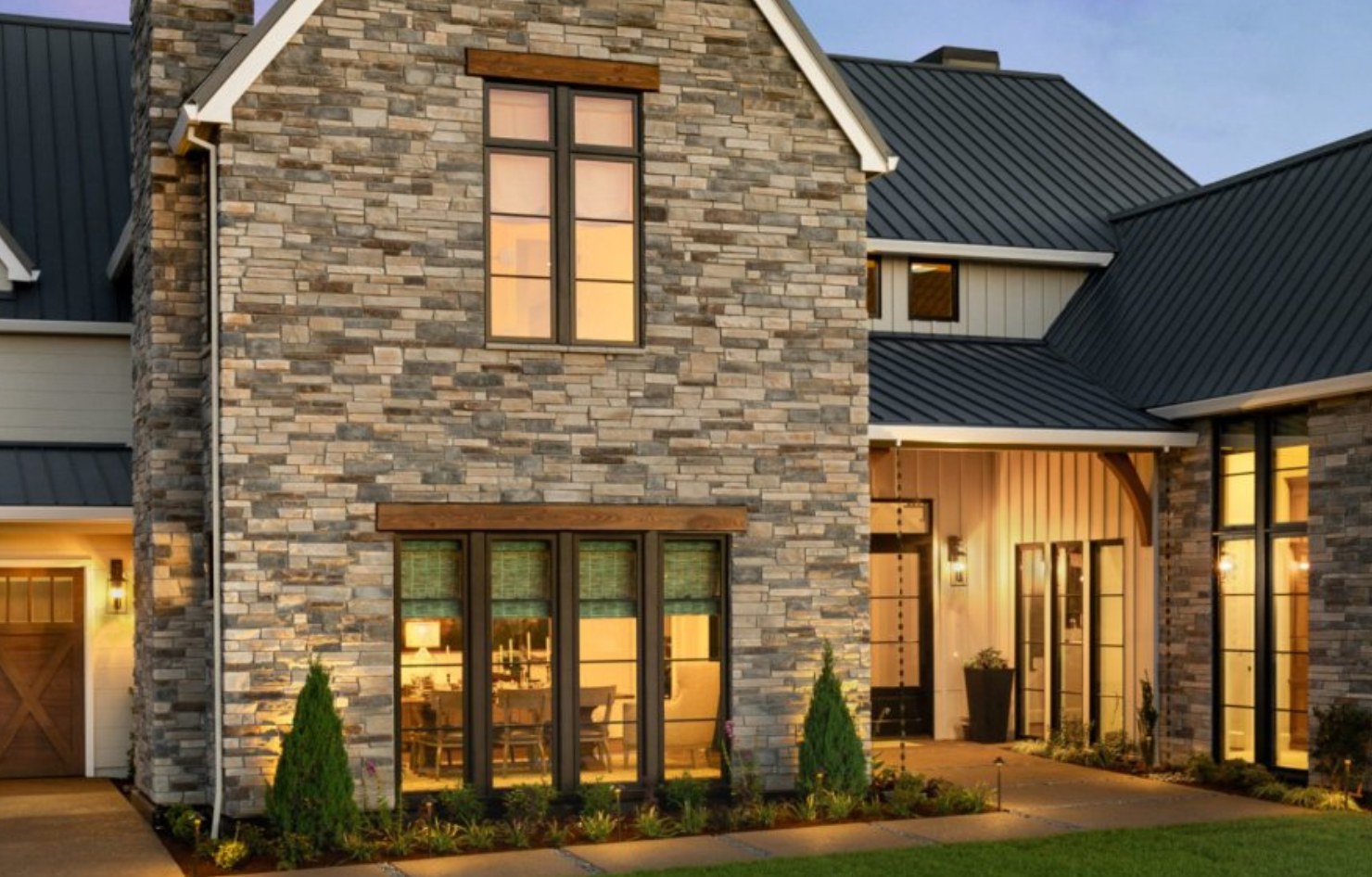 Modern farmhouse with Cultured Stone ledgestone veneer gable and chimney at dusk