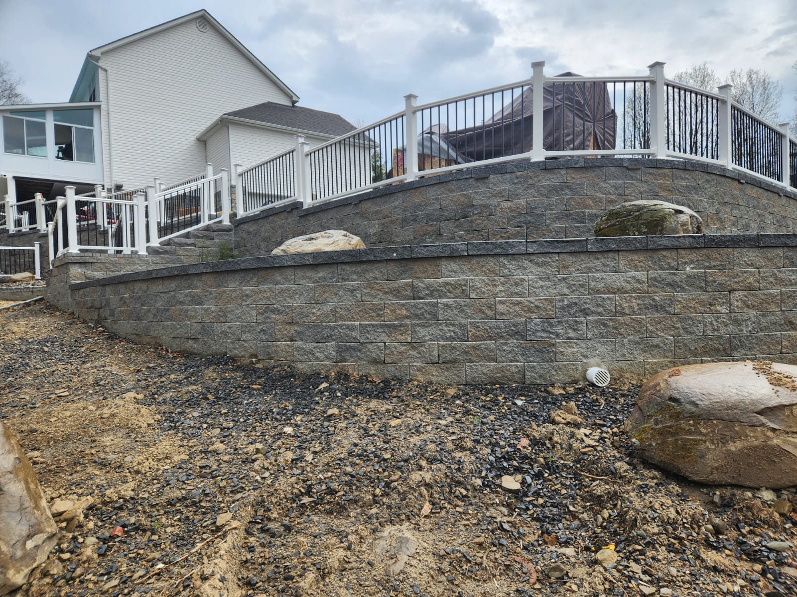 Curved retaining wall topped with deck railing and boulders