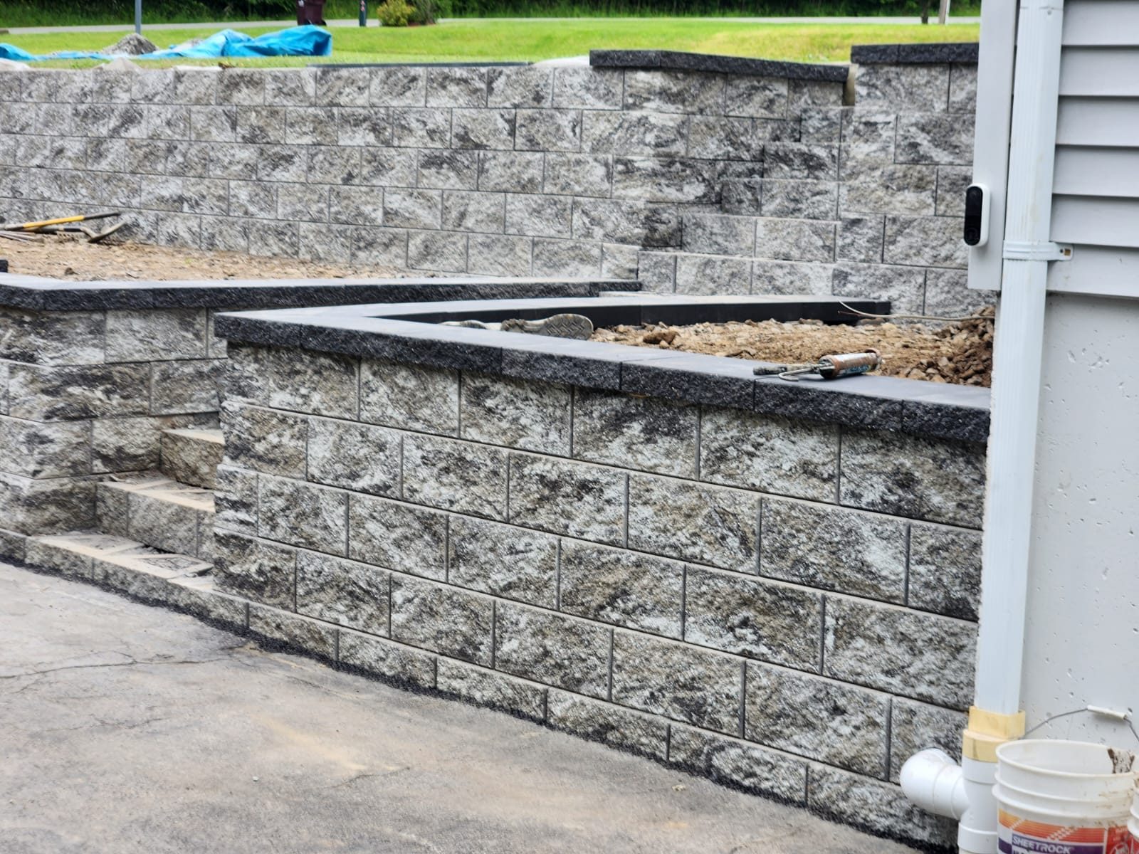 Tiered retaining wall with planter cutout and steps beside a house