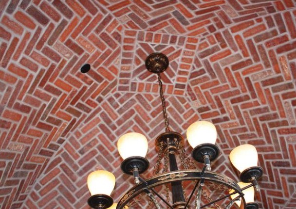 Vaulted ceiling finished in herringbone thin brick above a chandelier